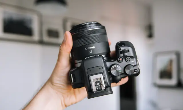 Dłoń trzyma aparat Canon z obiektywem 35mm, idealny dla amatora chcącego zacząć przygodę z fotografią.