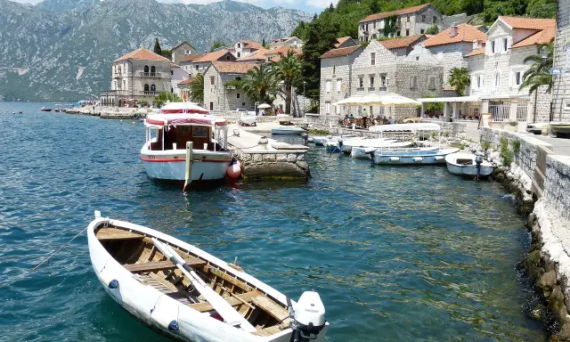 Port w Czarnogórze, łodzie na wodzie, góry w tle. Ceny rejsów mogą być różne, warto sprawdzić.