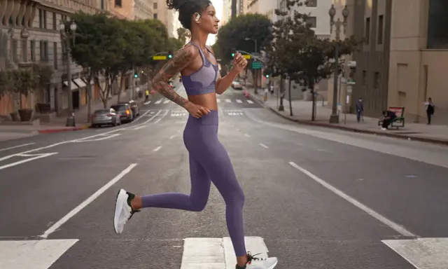 Donna in outfit viola, perfetto per come vestirsi in palestra, corre in strada.