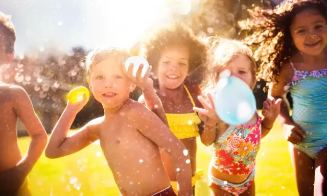 Niños riendo y jugando con globos de agua bajo el sol. Salpicaduras y diversión garantizada en estos juegos acuáticos.