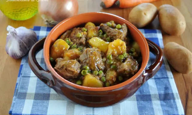 Un saporito spezzatino con patate e piselli, servito in una ciotola di terracotta, con ingredienti freschi sullo sfondo.