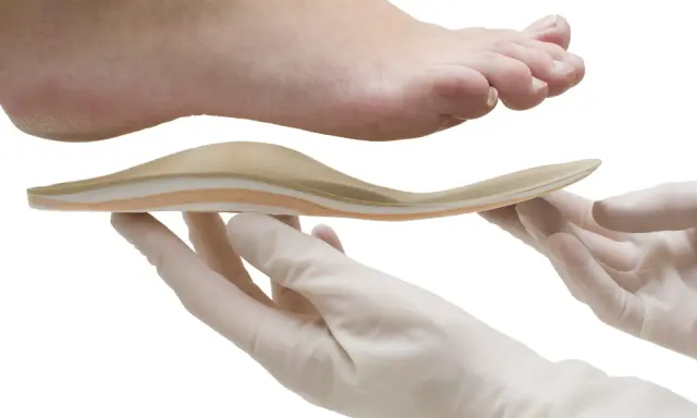 Une orthoplastie sur mesure est présentée sous un pied, tenue par des mains gantées.