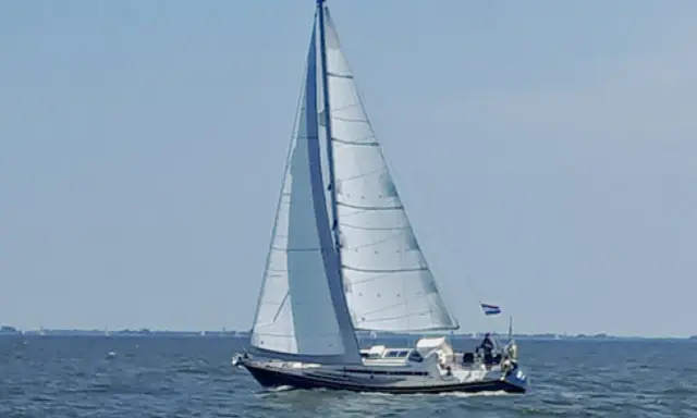 Voilier blanc et bleu naviguant sur une mer calme sous un ciel clair. Les voiles sont gonflées par le vent. Les premiers 375 avis sur ce type de bateau sont positifs.