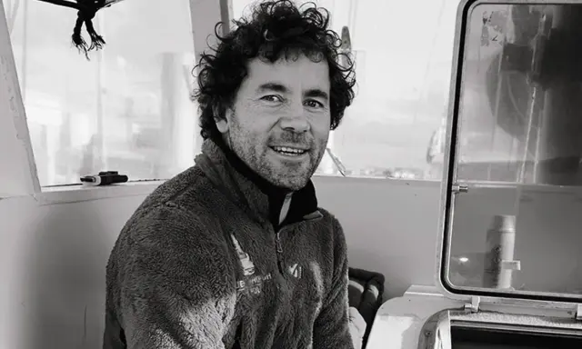Sébastien Roubinet, un aventurier souriant, pose à l'intérieur d'un bateau, prêt pour sa prochaine expédition.