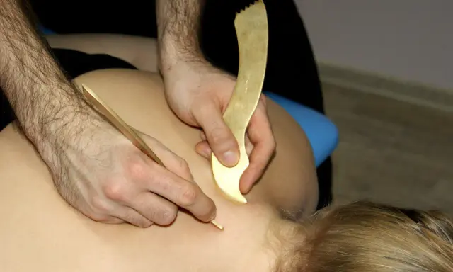 Terapeuta wykonuje zabieg pinopresury, używając złotych narzędzi do stymulacji punktów na plecach pacjenta.
