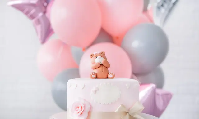 Uroczy topper na tort baby shower w kształcie misia siedzącego na różowym torcie, otoczony balonami w pastelowych kolorach.