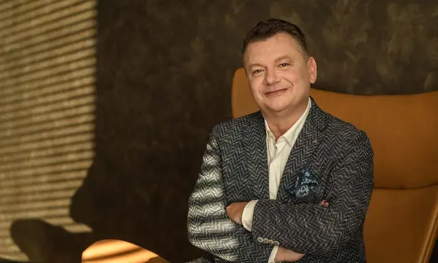 Uśmiechnięty mężczyzna, January Ciszewski, w eleganckiej marynarce siedzi w fotelu.