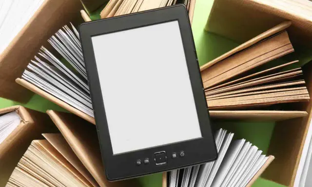 Un e-reader con schermo bianco è circondato da libri aperti, pronti per essere letti.