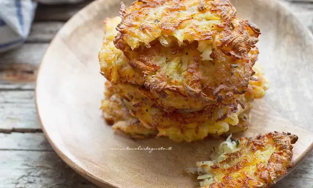 Una pila di dorate frittelle di patate su un piatto di legno. Croccanti fuori, morbide dentro, perfette per uno spuntino.