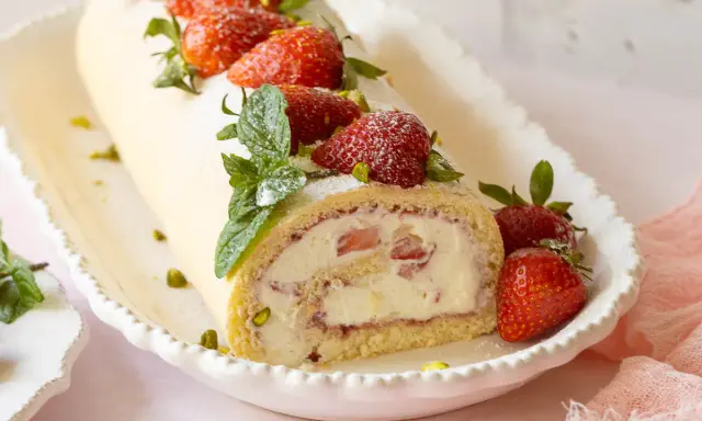 Eine köstliche Biskuitrolle mit Erdbeerfüllung, garniert mit frischen Erdbeeren, Minze und Pistazien. Ein süßer Genuss!