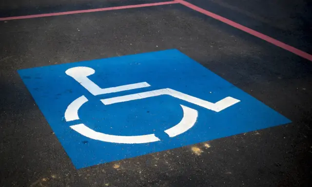 Niebieski kwadrat z białym symbolem wózka inwalidzkiego. To miejsce dla niepełnosprawnych na parkingu.