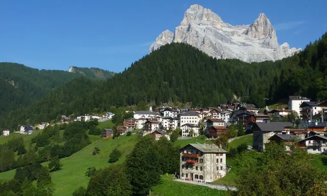 Villaggio alpino con case in pietra e legno, circondato da boschi e verdi pascoli, sotto un'imponente cima rocciosa. Il rifugio Venezia è un luogo incantevole.