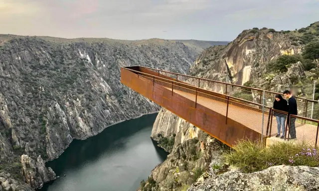 Pareja admira el paisaje desde el mirador del fraile, una pasarela metálica que se adentra en un cañón con un río.