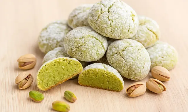 Amaretti pistache saupoudrés de sucre glace, avec des pistaches entières et décortiquées. Une recette gourmande à découvrir.