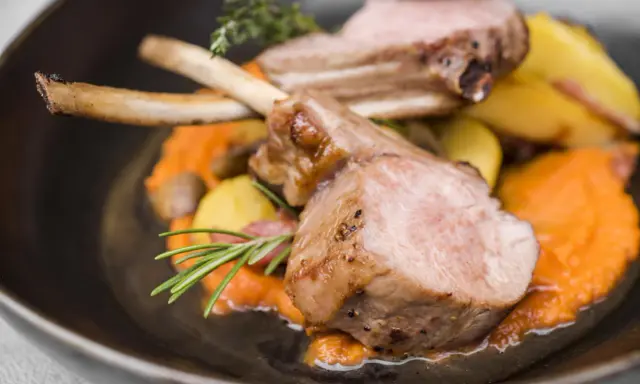 Chuleta de ternasco jugosa, servida sobre puré de zanahoria y patatas asadas, decorada con romero y tomillo.