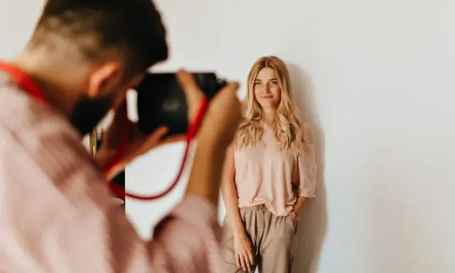 Fotograf robi zdjęcie uśmiechniętej blondynce. Zastanawiasz się, ile kosztuje sesja u fotografa?
