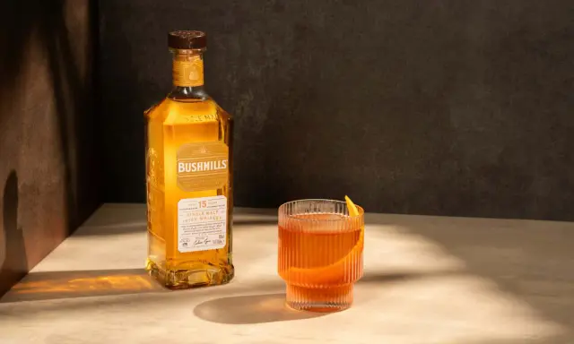 Butelka Bushmills 15 Year Old Single Malt Irish Whiskey obok szklanki z drinkiem. Wiele pozytywnych bushmills whisky opinie potwierdza jego wyjątkowy smak.