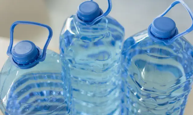 Trzy duże, niebieskie butelki z wodą, każda z uchwytem. Zastanawiasz się, ile może stać woda w plastikowej butelce po otwarciu?