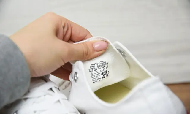 Dłoń pokazuje metkę z rozmiarem na białych butach Converse. Sprawdzamy, czy to oryginalne Converse, a nie podróbki.