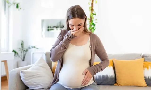 Donna incinta con nausea nel terzo trimestre, copre la bocca con la mano.