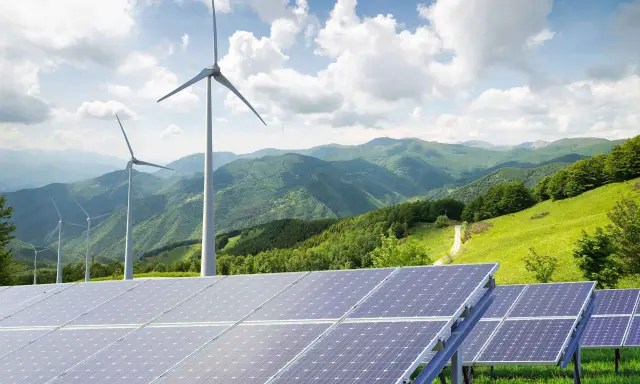 Paneles solares y aerogeneradores en un paisaje montañoso verde. La energía renovable, como la solar y la eólica, complementa la idea de un futuro sostenible, similar a cómo un generador de biomasa podría integrarse.