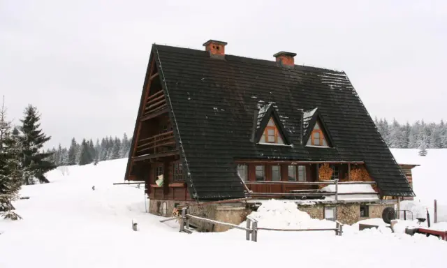 Drewniana bacówka w zimowej scenerii, otoczona śniegiem i lasem.
