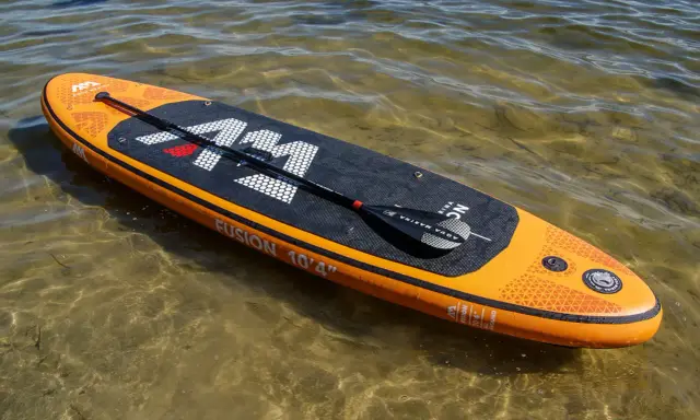 Pomarańczowy aquamarina sup z wiosłem leży na płytkiej, przejrzystej wodzie.