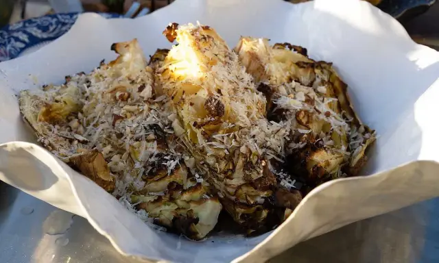 Grillad spetskål serverad i en vit skål, toppad med riven ost och hackade nötter. En härlig rätt för grillkvällen.