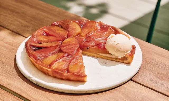 Tarte Tatin caramélisée, une part coupée, servie avec une boule de glace à la vanille. La cuisson parfaite révèle des pommes dorées et une pâte croustillante.
