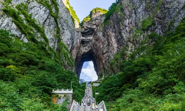 Eine lange Treppe führt durch eine Schlucht mit üppiger Vegetation hinauf zu einem riesigen Felsentor, den "Stairs to Heaven" in China.