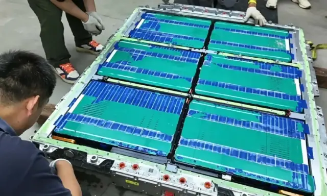 Un tecnico lavora su un pacco batteria, con celle verdi e blu che ricordano una blade battery.