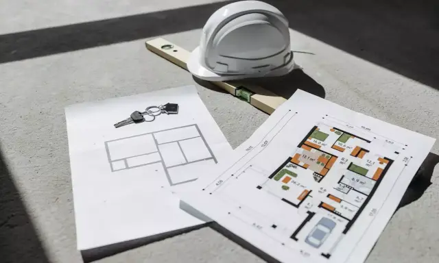Clés, casque et niveau à bulle sur des plans d'architecte, un aperçu d'un projet de construction. Un plan architecte gratuit pour concrétiser vos rêves.