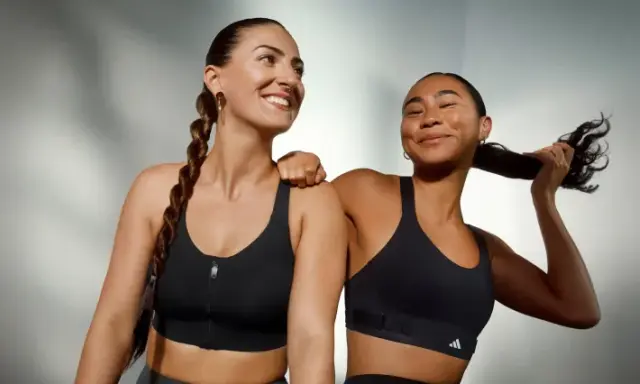 Two women in black sports bras, one with a braid, the other playing with her hair.