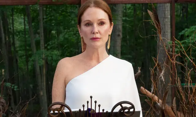 Julianne Moore i den vita klänningen i "Sirens"-serien, med en bakgrund av skog och dekorationer av fjädrar och kvistar.