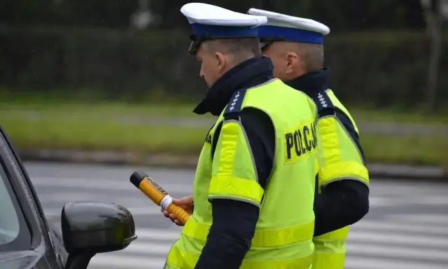 Policjant w kamizelce odblaskowej trzyma alkomat. Czy policja może badać alkomatem w domu? To pytanie często zadawane przez kierowców.