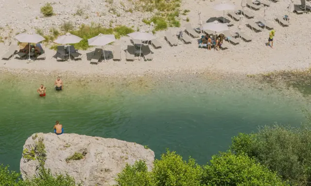 Wczasy w Albanii: ludzie odpoczywają na plaży nad krystalicznie czystą wodą, niektórzy kąpią się, inni relaksują pod parasolami.