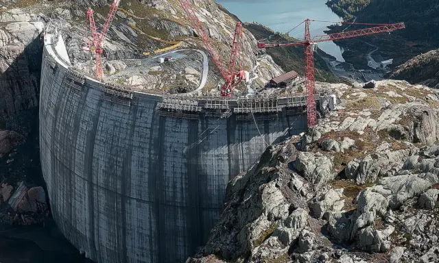 Bau einer gewaltigen Staumauer, die an Pumpspeicherkraftwerke in Deutschland erinnert. Kräne ragen in den Himmel, während die Betonkonstruktion wächst.