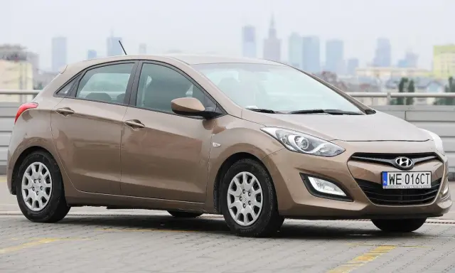 Brązowy Hyundai i30 1.6 benzyna na parkingu z widokiem na miasto w tle.