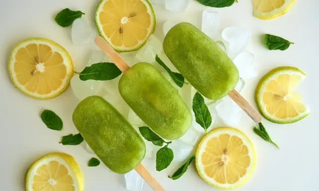Trois bâtonnets glacés verts, comme une coupe colonel rafraîchissante, entourés de citrons, de menthe et de glaçons.