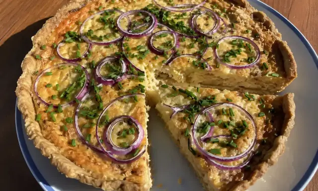 En gyllene ostpaj med rödlök och gräslök, perfekt för ett ostpaj recept. En bit är uppskuren.
