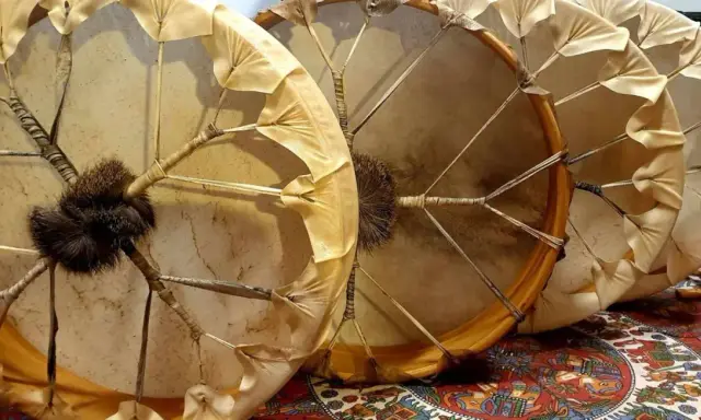 Trois tambours chamaniques, un instrument traditionnel aux peaux tendues et ornées de franges, prêts pour une cérémonie.
