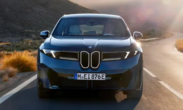 Der BMW iX4 fährt auf einer kurvigen Straße durch eine bergige Landschaft im goldenen Licht der Abendsonne.