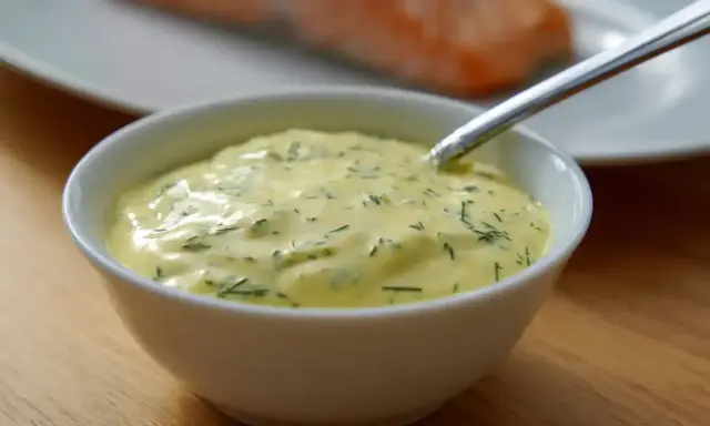 En skål med krämig romsås till lax, med dill och en sked redo att servera.