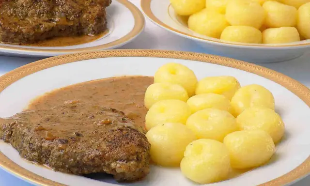 Pyszna karkówka w sosie, podana z kluskami śląskimi. Danie wygląda apetycznie i zachęca do spróbowania.