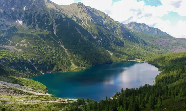 Górskie jezioro otoczone lasem, z wodospadem spływającym po zboczu. Widok przypomina, jak powstało Morskie Oko.