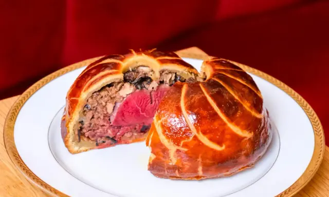 Un pâté en croûte aux couches généreuses, un délice d'antan origine, sur une assiette blanche bordée d'or.