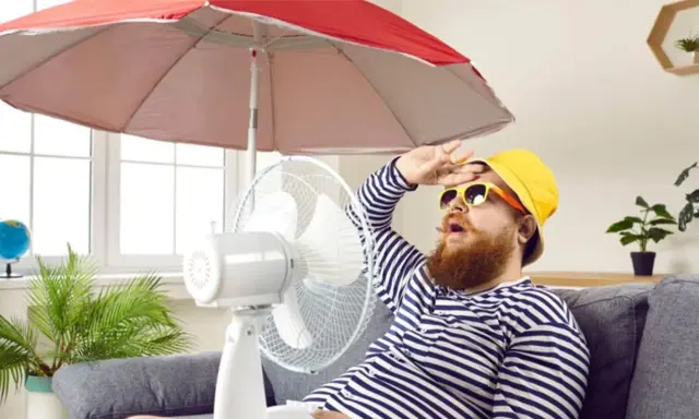 Un homme transpire sous un parasol, ventilateur et plante pour comment rafraichir sa maison. Il a chaud.
