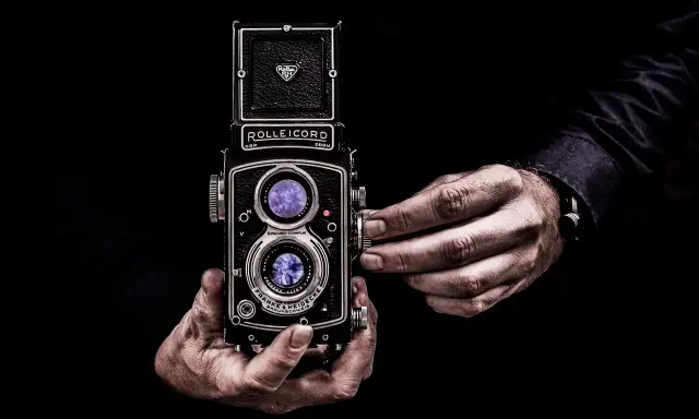 Dwie ręce trzymają aparat Rolleiflex, jedna reguluje ostrość. Sztuka fotografii, zasada złotego środka w kadrze.
