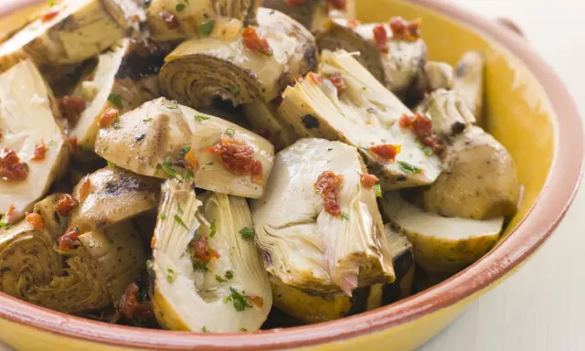 Ein köstlicher Artischockensalat mit getrockneten Tomaten und Kräutern in einer gelben Schüssel.