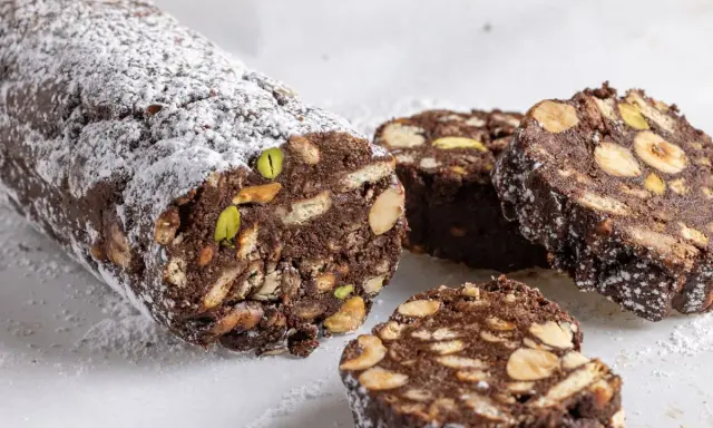 Salame di cioccolato senza uova ricetta della nonna, con biscotti, nocciole e pistacchi, spolverato di zucchero a velo.